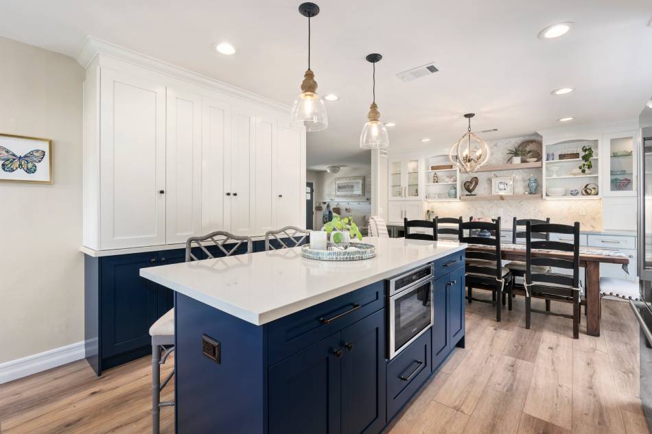 Stylish kitchen with blue countertop, hanging simple chandeliers, and white house motif.